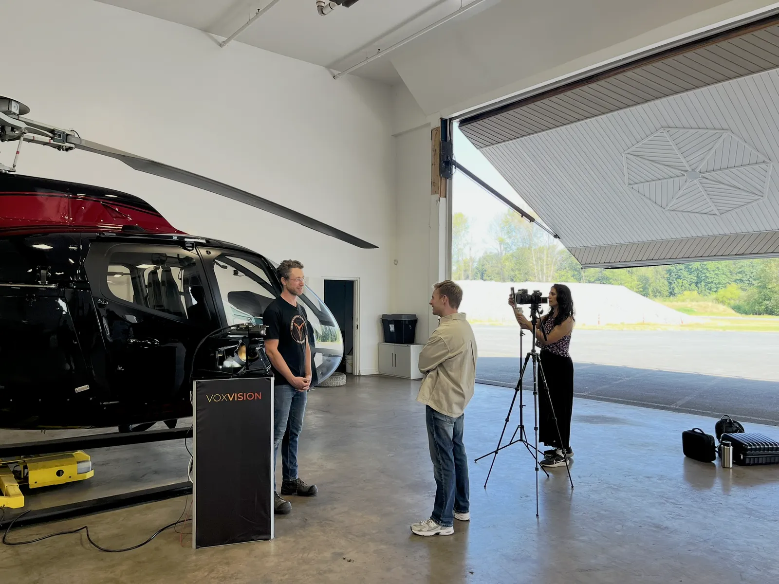 An interview being filmed beside a helicopter and VoxVision equipment in a hangar.